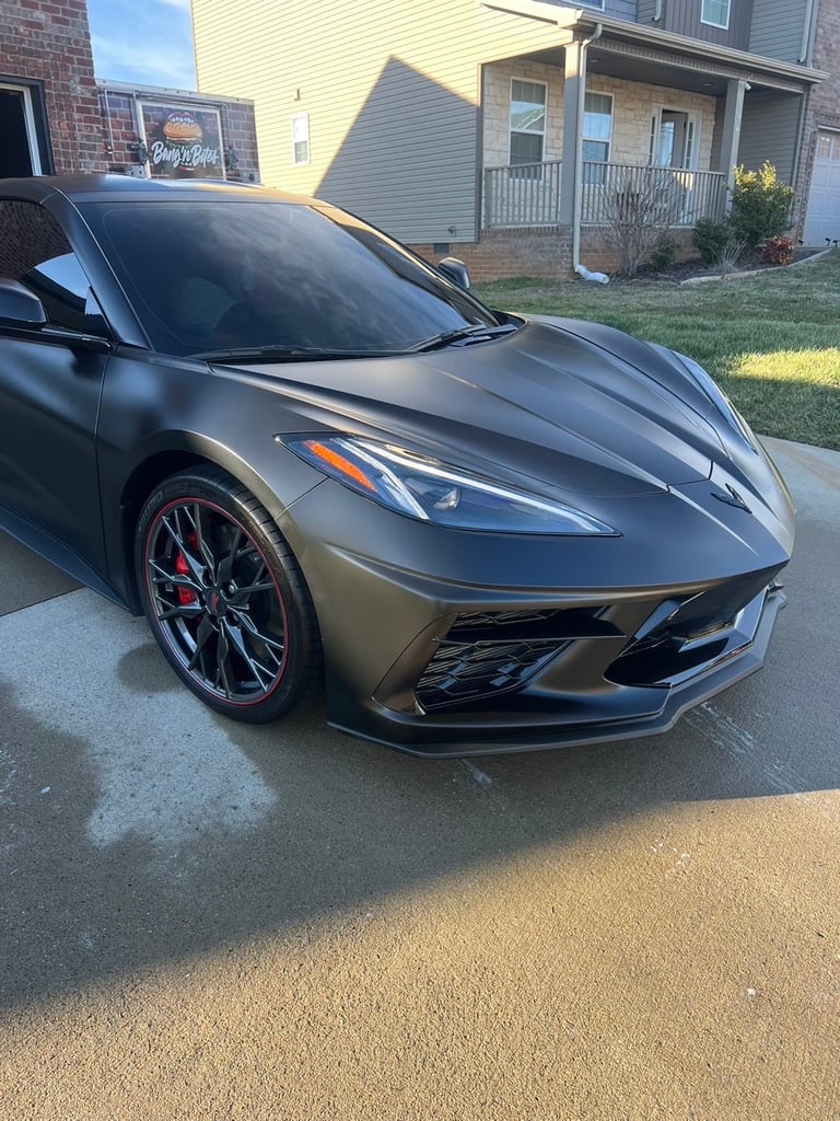 Gray sports car with red accents parked in a driveway, with houses visible in the background
