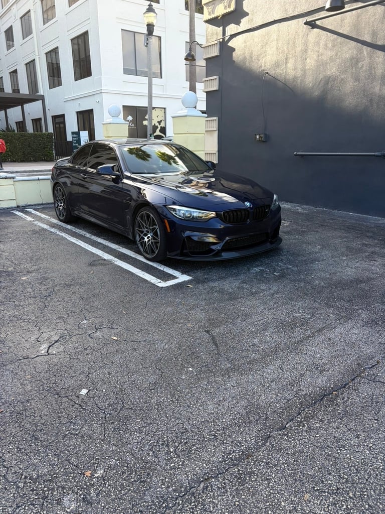 Black BMW sports car parked in urban parking lot near modern white building and black wall
